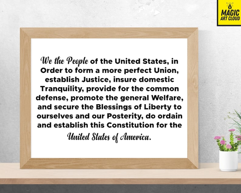May include: A framed print of the Preamble to the United States Constitution. The text is in black font on a white background. The frame is a light wood colour.