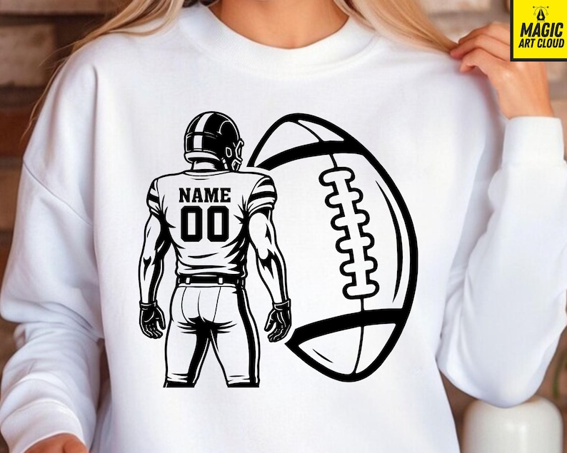 Puede incluir: Sudadera blanca con un gr&aacute;fico en blanco y negro de un jugador de f&uacute;tbol americano y un bal&oacute;n. La camiseta del jugador muestra "NAME" sobre el n&uacute;mero "00". El bal&oacute;n tambi&eacute;n es blanco y negro. Dise&ntilde;o gr&aacute;fico audaz.
