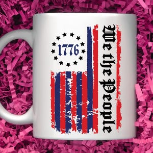 May include: White ceramic mug featuring a distressed American flag design. The flag has red and blue stripes with white stars in the top left corner. The text "We the People" is printed vertically on the right side of the flag. The year "1776" is printed in the centre of the stars.