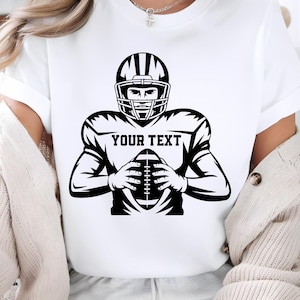 Puede incluir: Camiseta blanca con un gr&aacute;fico en blanco y negro de un jugador de f&uacute;tbol americano con casco, sosteniendo un bal&oacute;n de f&uacute;tbol. El texto "YOUR TEXT" se muestra en el pecho del jugador.