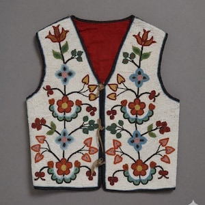 Puede incluir: Un chaleco sin mangas con fondo blanco cubierto de intrincados abalorios que representan motivos florales en rojo, azul, verde y amarillo. La prenda tiene un forro interior de color rojo oscuro y se abrocha en la parte delantera con tres lazos beige.