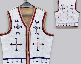 May include: A sleeveless vest featuring white beadwork with geometric patterns in blue, red, and light blue. The garment has a tan interior lining, a V-neckline, and a front tie closure. The back displays a matching pattern with blue and red accents.