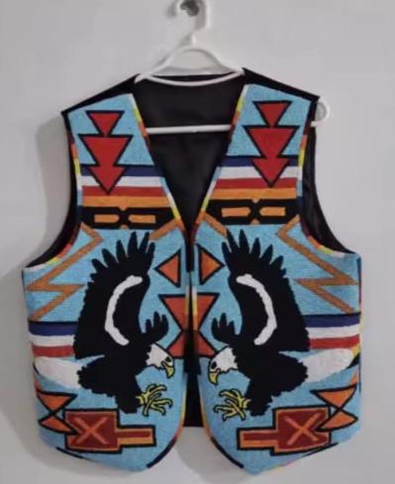 Puede incluir: Un chaleco con cuentas con un reverso negro, colgado de una percha blanca. El dise&ntilde;o presenta dos &aacute;guilas negras sobre un fondo azul claro. Los patrones geom&eacute;tricos en rojo, naranja y blanco completan el dise&ntilde;o.