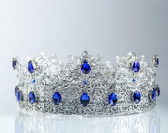 Peut inclure: Une couronne argentée avec des détails de filigrane complexes. Elle est ornée de nombreux grands joyaux bleus profonds de forme ovale. Le design est symétrique, avec des pierres précieuses espacées régulièrement. La couronne est probablement pour des occasions spéciales.