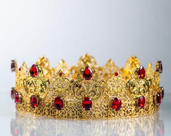 Puede incluir: Una corona dorada con intrincados detalles de filigrana y numerosos acentos de piedras preciosas rojas. El diseño de la corona presenta patrones ornamentados y probablemente está destinado a fines ceremoniales o decorativos.