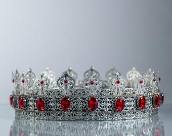Peut inclure: Une couronne argentée avec des détails de filigrane complexes et des pierres précieuses rouges vives. La couronne présente une série de croix ornées et est conçue avec une surface réfléchissante, créant une apparence royale et élégante. Idéal pour les événements.
