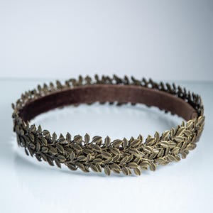 Puede incluir: Una diadema circular que presenta una banda continua de hojas met&aacute;licas en tono bronce. El exterior est&aacute; compuesto por motivos de hojas detallados y superpuestos, mientras que el interior est&aacute; forrado con un tejido liso de color marr&oacute;n oscuro.