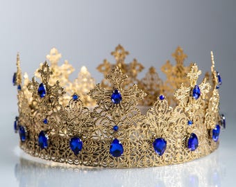 Puede incluir: Una corona dorada con intrincados detalles de filigrana y gemas azules en forma de lágrima. La corona tiene un diseño simétrico con múltiples puntas y probablemente está destinada a fines ceremoniales o decorativos.