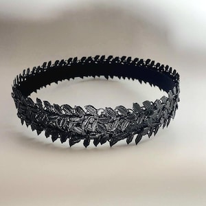 Puede incluir: Una corona de hojas negra, con intrincados detalles de hojas. La corona est&aacute; hecha de un material oscuro y est&aacute; dise&ntilde;ada para ser usada alrededor de la cabeza. Las hojas est&aacute;n dispuestas en un patr&oacute;n circular, creando un adorno para la cabeza decorativo.