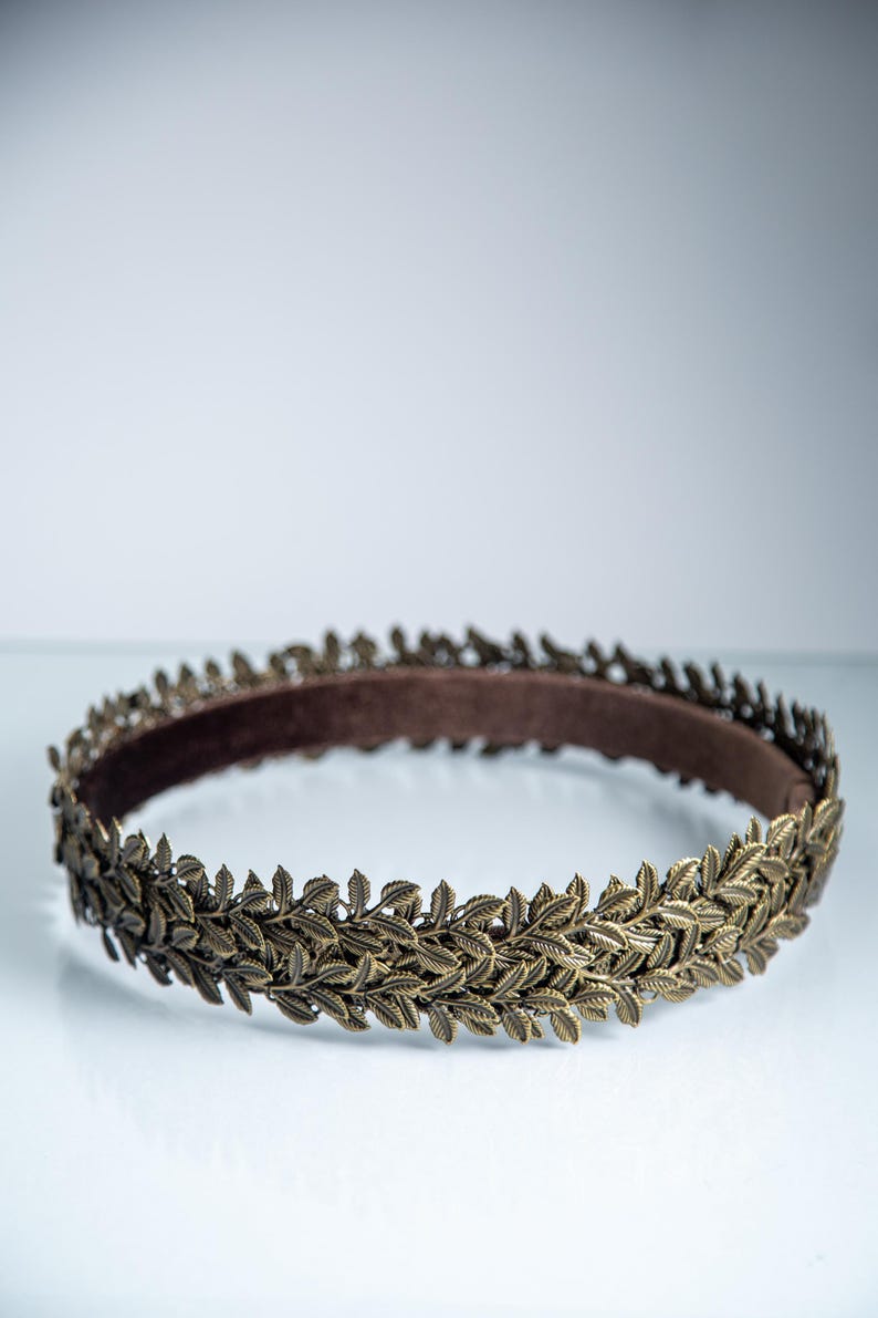 Puede incluir: Una diadema circular que presenta una banda continua de hojas met&aacute;licas en tono bronce. El exterior est&aacute; compuesto por motivos de hojas detallados y superpuestos, mientras que el interior est&aacute; forrado con un tejido liso de color marr&oacute;n oscuro.