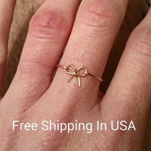 May include: A gold-toned ring with a delicate bow design. The ring is worn on a finger.