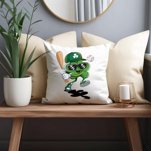 May include: A white cushion featuring a green shamrock wearing sunglasses and a baseball cap, holding a baseball bat. The shamrock is smiling and has a baseball behind it.