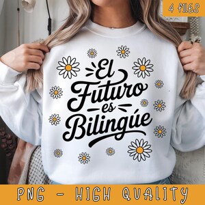 以下が含まれることがあります： 白いスウェットシャツ。黒い文字で「El Futuro es Bilingüe」と書かれており、デイジーのグラフィックで囲まれています。スウェットシャツには、黄色のバナーに「PNG - HIGH QUALITY」という文字も書かれています。
