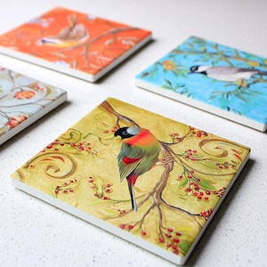 May include: Four square ceramic coasters with bird illustrations. Each coaster features a different bird design on a colorful background. The coasters have white edges and are suitable for home decor.