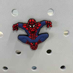 Peut inclure: Un charm de chaussure en caoutchouc souple repr&eacute;sentant le personnage Spider-Man dans une pose accroupie. Le design affiche le costume embl&eacute;matique rouge et bleu avec un motif de toile noir, des yeux blancs et un embl&egrave;me d'araign&eacute;e noir sur le torse.