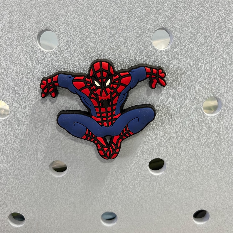 Peut inclure: Un charm de chaussure en caoutchouc souple repr&eacute;sentant le personnage Spider-Man dans une pose accroupie. Le design affiche le costume embl&eacute;matique rouge et bleu avec un motif de toile noir, des yeux blancs et un embl&egrave;me d'araign&eacute;e noir sur le torse.
