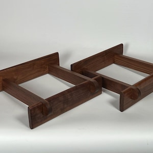 May include: Two wooden display stands. Each stand is rectangular with a square opening in the center. The stands are made of dark brown wood and have a minimalist design. The stands are likely for displaying items.