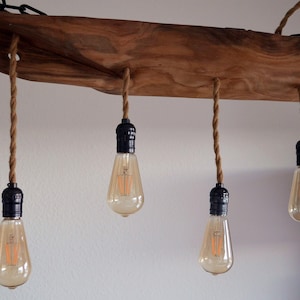Puede incluir: Una lámpara de madera rústica con cuatro bombillas colgantes. La lámpara está hecha de una gruesa pieza de madera con un acabado natural. Las bombillas son de estilo Edison con vidrio transparente y un brillo cálido.