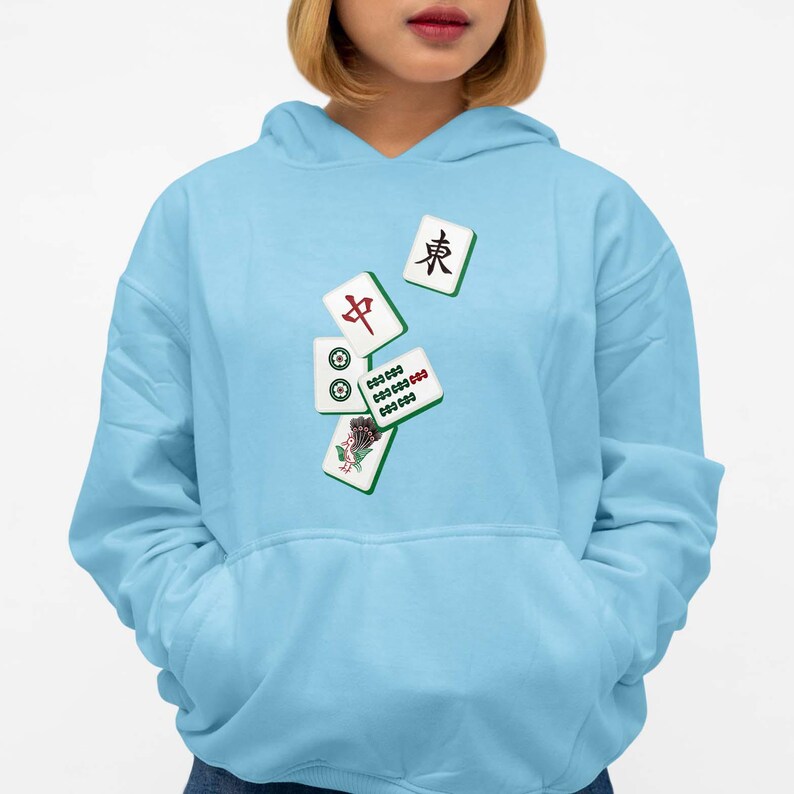 Puede incluir: Sudadera con capucha azul claro con un dise&ntilde;o de fichas de Mahjong. Las fichas son blancas con s&iacute;mbolos rojos, verdes y negros. La sudadera tiene un bolsillo delantero y una capucha con cord&oacute;n.