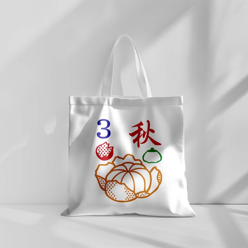 May include: White tote bag with a colorful graphic design. The design includes the number 3 in blue, Chinese characters in red, and illustrations of a fruit and a vegetable. The bag has a simple, clean design.