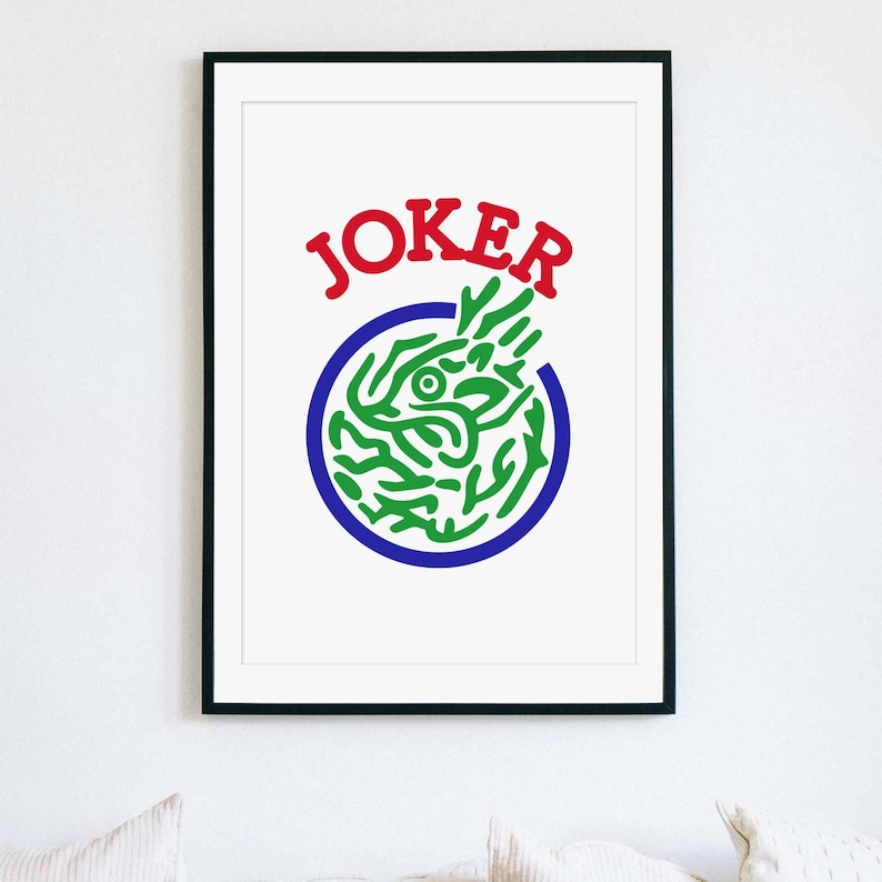 May include: Framed art print featuring the word "JOKER" in red above a green and blue graphic. The graphic is a stylized design within a blue circle, set against a white background. The artwork is framed in a black frame.