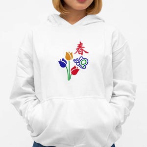 May include: White hoodie featuring a colorful floral and butterfly design with the Chinese character for "spring". The graphic includes blue, yellow, and red tulips with green stems. The design is centered on the front of the hoodie.