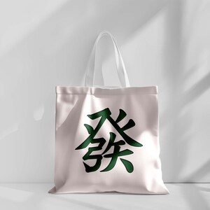 Puede incluir: Un bolso tote de color rosa claro con asas blancas. El bolso presenta un gran car&aacute;cter chino verde oscuro en el centro. El bolso est&aacute; hecho de un material suave y duradero, adecuado para transportar varios art&iacute;culos.