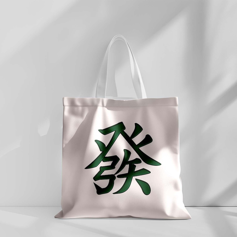 Puede incluir: Un bolso tote de color rosa claro con asas blancas. El bolso presenta un gran car&aacute;cter chino verde oscuro en el centro. El bolso est&aacute; hecho de un material suave y duradero, adecuado para transportar varios art&iacute;culos.