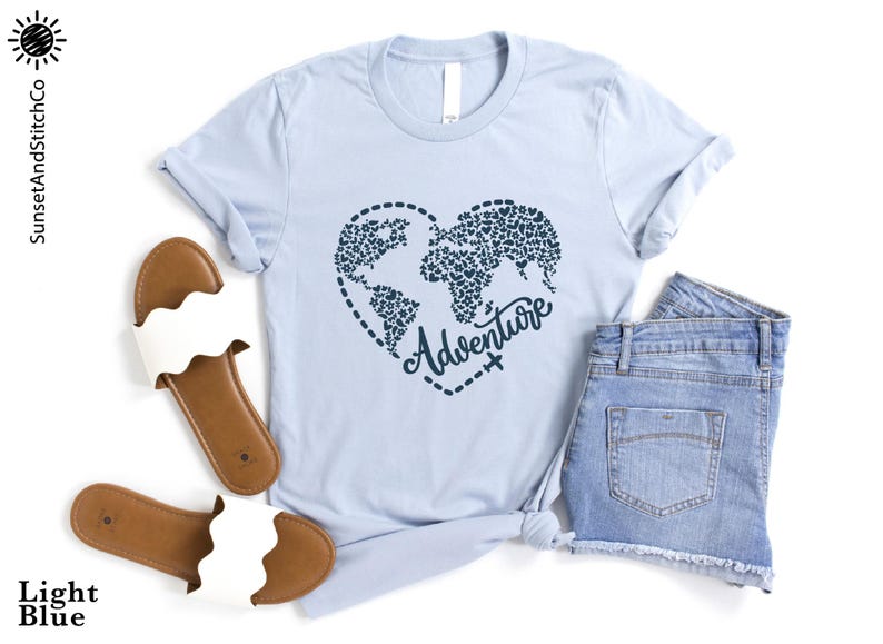 May include: Light blue t-shirt with a heart-shaped world map design, the word "Adventure" in script, and a pair of denim shorts. Sandals with white straps and brown soles are also in the image.