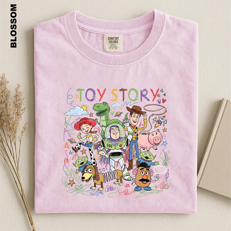 A pink t-shirt with a colorful graphic design featuring characters from the Toy Story movie, including Woody, Buzz Lightyear, and Piggy.