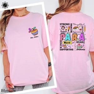 A woman wearing a pink t-shirt with a colorful graphic design and text on the back.