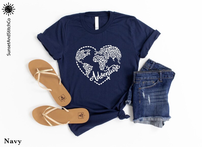 May include: Navy blue t-shirt with a white heart-shaped world map design and the word "Adventure". The shirt is paired with denim shorts and tan sandals. The image is set against a white background.