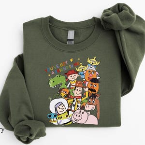A green sweatshirt with a colorful graphic of various cartoon characters from the Toy Story franchise, including Woody, Buzz Lightyear, and other beloved characters.