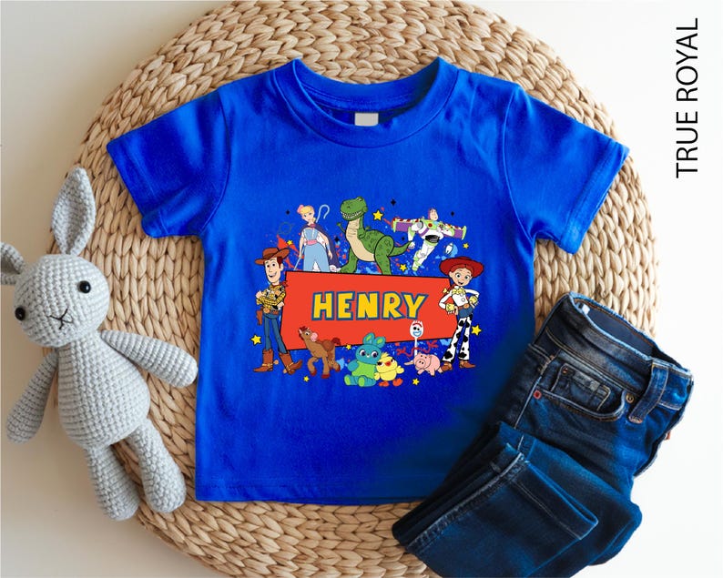 A blue t-shirt with a cartoon character design and the name "Henry" printed on it, along with a pair of jeans and a stuffed rabbit toy.