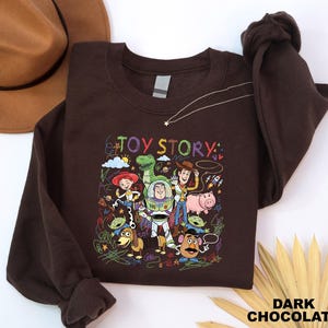 A brown sweatshirt with a colorful graphic of characters from the Toy Story movie, including Woody, Buzz Lightyear, and other beloved characters, along with the text "TOY STORY".