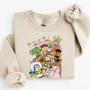 A beige sweatshirt with a colorful graphic design featuring various cartoon characters from the Toy Story franchise.