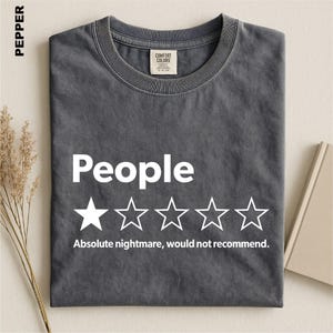 May include: A charcoal gray crew neck t-shirt featuring the white text "People" above a graphic of five stars, with only the first star filled in. Below the stars, the white text reads "Absolute nightmare, would not recommend."