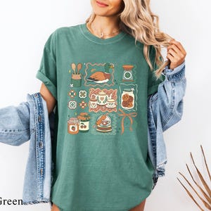 A woman wearing a green t-shirt with a graphic design of various objects, including a bird, a jar, and a plant, standing in front of a plant.
