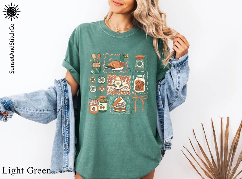 A woman wearing a green t-shirt with a graphic design of various objects, including a bird, a jar, and a plant, standing in front of a plant.