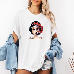 A woman wearing a white t-shirt with a colorful graphic of a woman's face and floral elements.