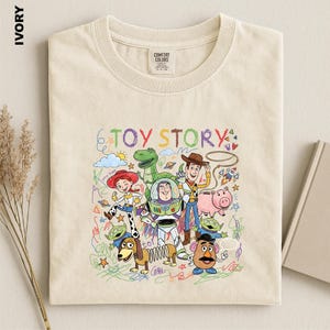 A beige t-shirt with a colorful illustration of characters from the Toy Story movie, including Woody, Buzz Lightyear, and other beloved characters.