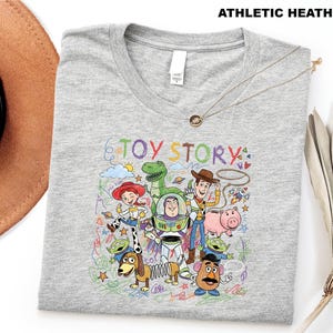 A gray t-shirt with a colorful graphic design featuring characters from the Toy Story movie, including Woody, Buzz Lightyear, and other beloved characters.