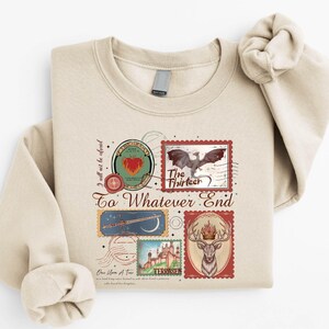 A beige sweatshirt with a printed design featuring various elements such as a bird, a castle, and a heart.