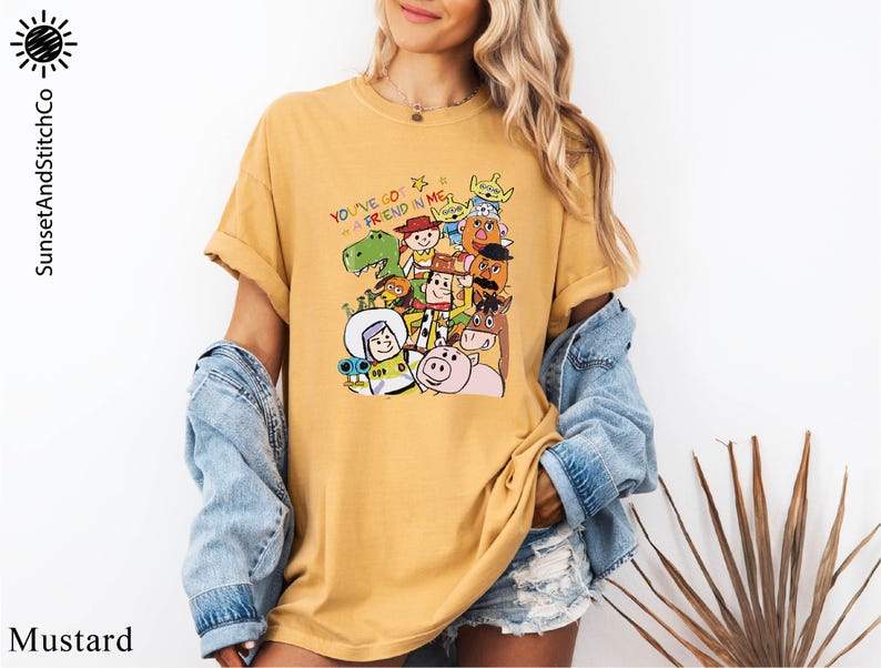 A woman wearing a yellow t-shirt with a colorful graphic of various cartoon characters, including a pig, a dinosaur, and a robot. She is also wearing a denim jacket and denim shorts.