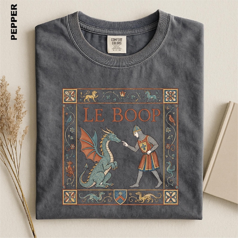 May include: A charcoal gray crew neck t-shirt featuring a medieval-style graphic print. The design shows a knight touching a dragon's nose with the text LE BOOP, surrounded by a decorative floral border and small mythical creatures.