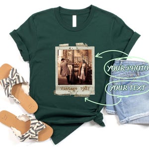 May include: Forest green t-shirt with a vintage photo graphic. The photo shows a couple walking, with the text "Vintage 1987" below. The shirt is styled with sandals and denim shorts.