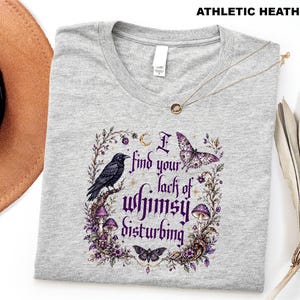 Puede incluir: Una camiseta gris jaspeado athletic heather con un estampado gr&aacute;fico que incluye el texto I find your lack of whimsy disturbing. El dise&ntilde;o presenta un cuervo negro, setas moradas, una mariposa, una polilla y elementos florales en tonos morados.