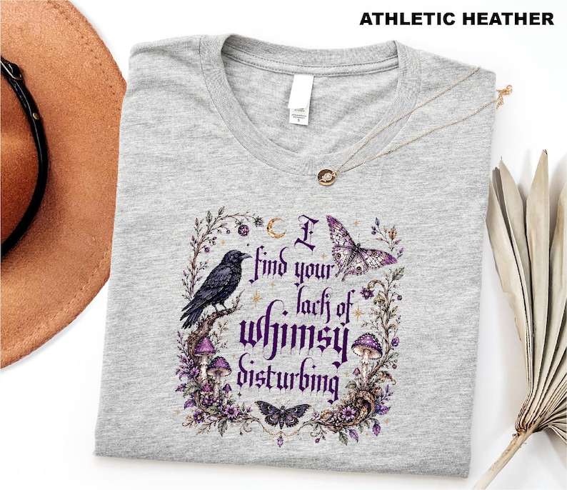 Puede incluir: Una camiseta gris jaspeado athletic heather con un estampado gr&aacute;fico que incluye el texto I find your lack of whimsy disturbing. El dise&ntilde;o presenta un cuervo negro, setas moradas, una mariposa, una polilla y elementos florales en tonos morados.