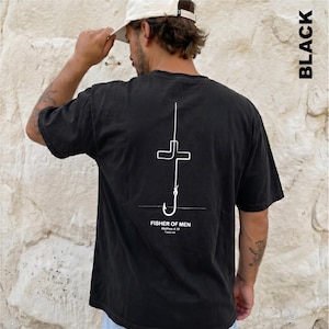 May include: A black short-sleeve t-shirt featuring a white line art graphic on the back. The design depicts a fishing hook shaped like a cross with the text "FISHER OF MEN", "Matthew 4:19", and "Follow me" printed underneath the graphic.