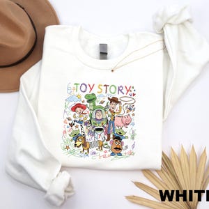 A white long-sleeved shirt with a colorful illustration of characters from the Toy Story movie, including Woody, Buzz Lightyear, and other beloved characters.